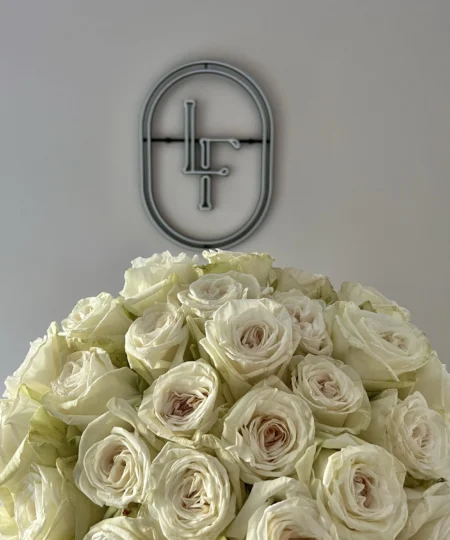 Close-up of full White O’Hara roses with creamy white petals and soft blush centers, placed below the Lu La Fleur neon logo
